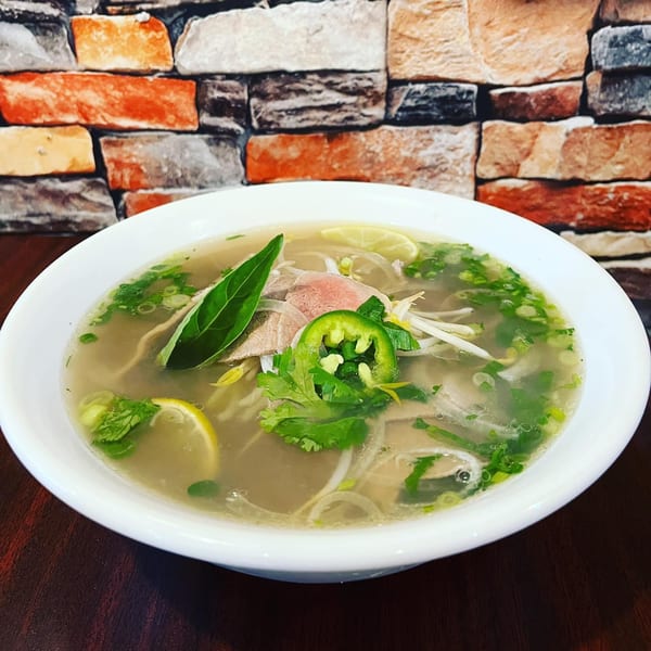 A bowl of Vietnamese pho with beef, noodles, herbs, lime, and jalapeños.