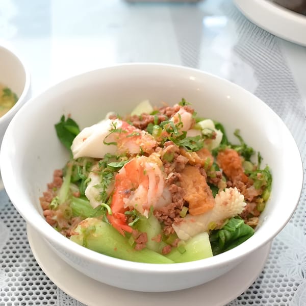A bowl of Vietnamese seafood and pork stir-fry with green vegetables and herbs.