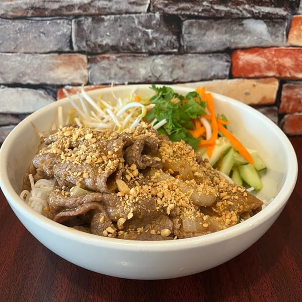 Vietnamese vermicelli bowl with beef, peanuts, bean sprouts, and pickled vegetables against a brick wall.